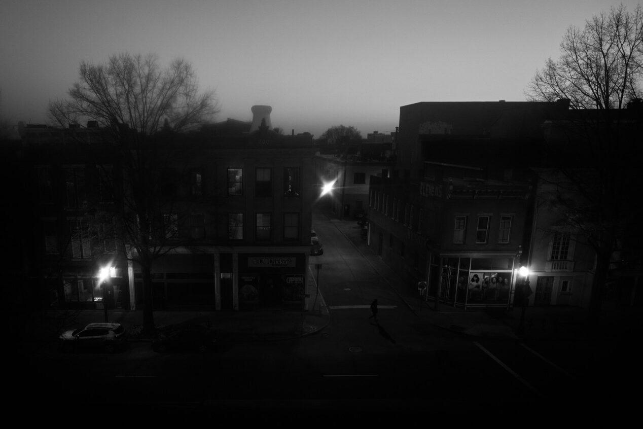 Tree branches etched against a winter sky, stark and lyrical, above a cityscpe with three contrasting lights.