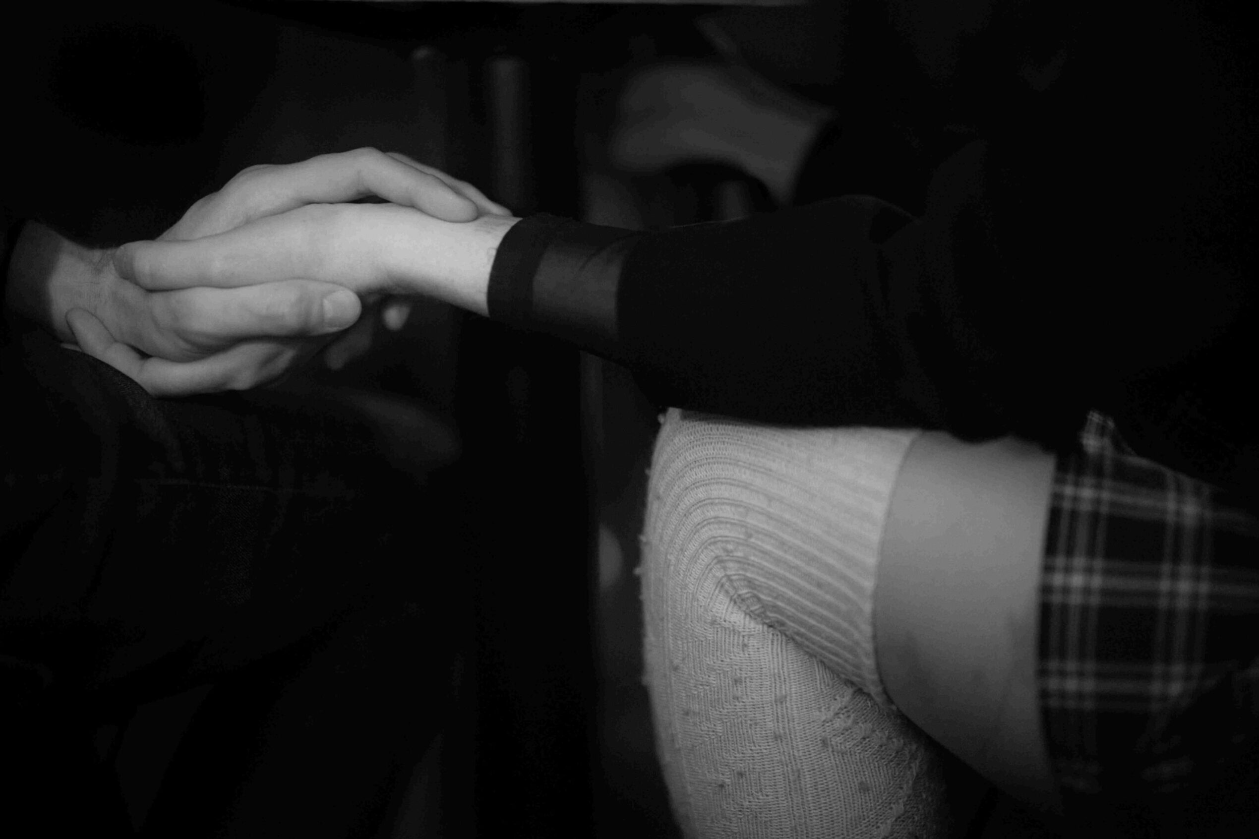 Two seated people holding hands, captured at knee level.