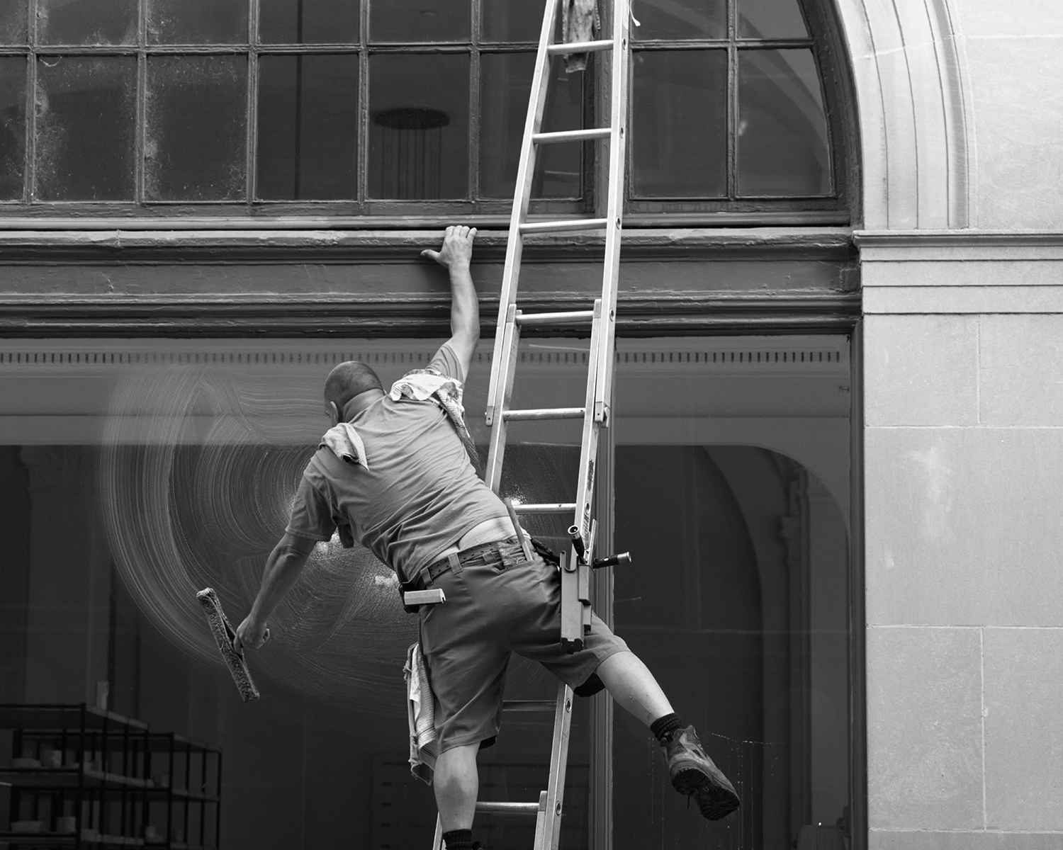 Window cleaner leaning over a bowed latter to reach the hard spots.